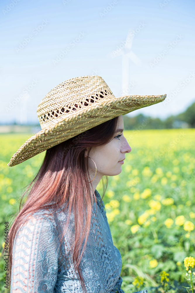 Obraz premium White girl with dark hair in straw hat with sky behind in meadow