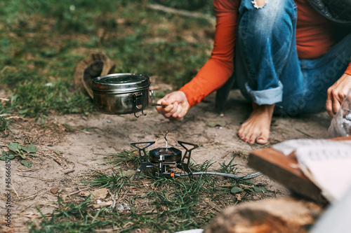 A woman cooks food with a portable gas burner in the forest