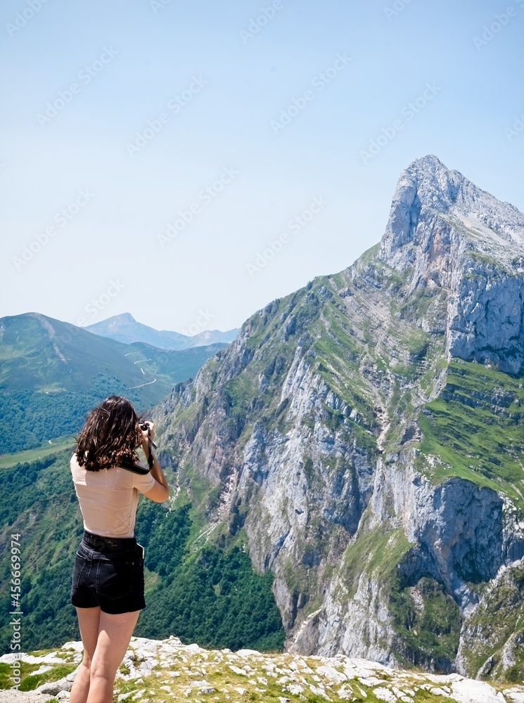 Naklejka premium Rear view of a young woman taking photos of a rocky peak