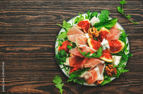 Fig salad with prosciutto, blue cheese, walnuts, arugula on old wooden background, top view, copy space