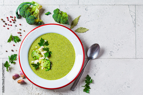 Broccoli soup puree in plate on gray tile background with ingredients. Cooking healthy food concept.