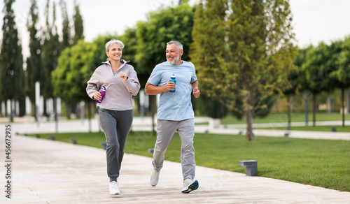 Bild auf Leinwand Full-length photo of lovely joyful retirees couple jogging outside in city park