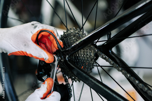 Obraz na plátně close - up of the male mechanic working in the bicycle repair shop, mechanic repairing bike using a special tool, wearing protective gloves