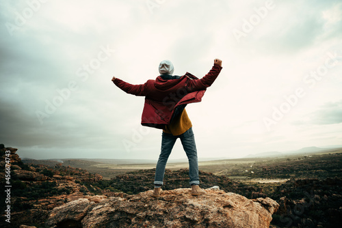 Caucasian male hiker standing on top of mountain with open arms successfully reaching mountain peak 