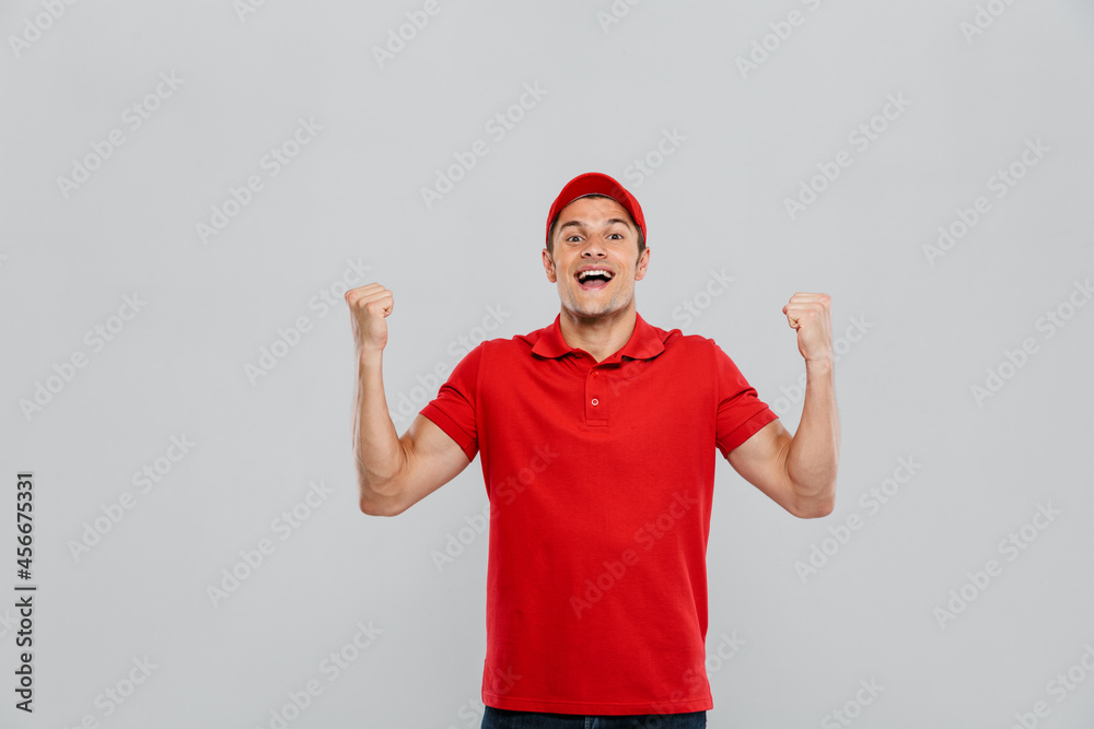 Young delivery man wearing uniform screaming while making winner gesture Young delivery man wearing uniform screaming while making winner gesture