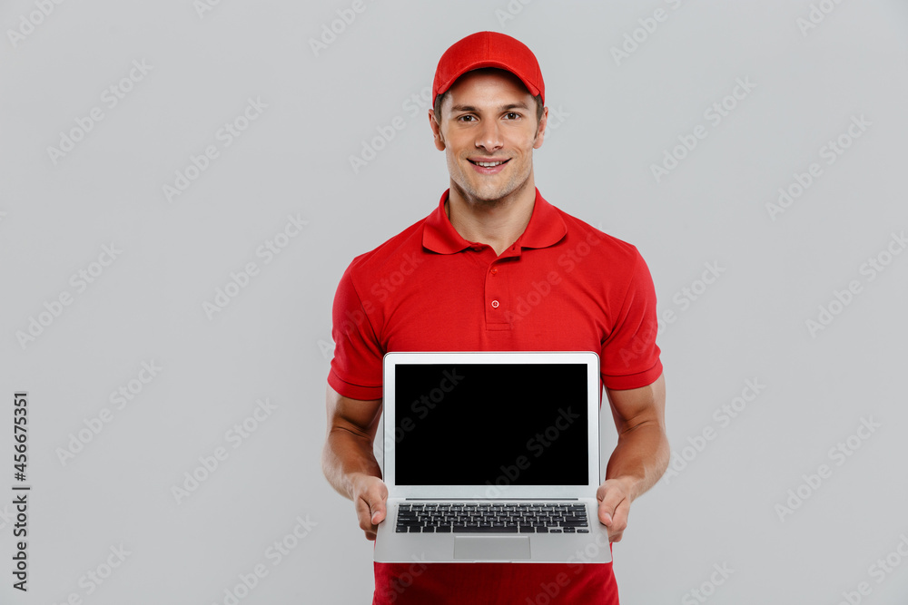 Young delivery man in uniform smiling while showing laptop Young delivery man in uniform smiling while showing laptop