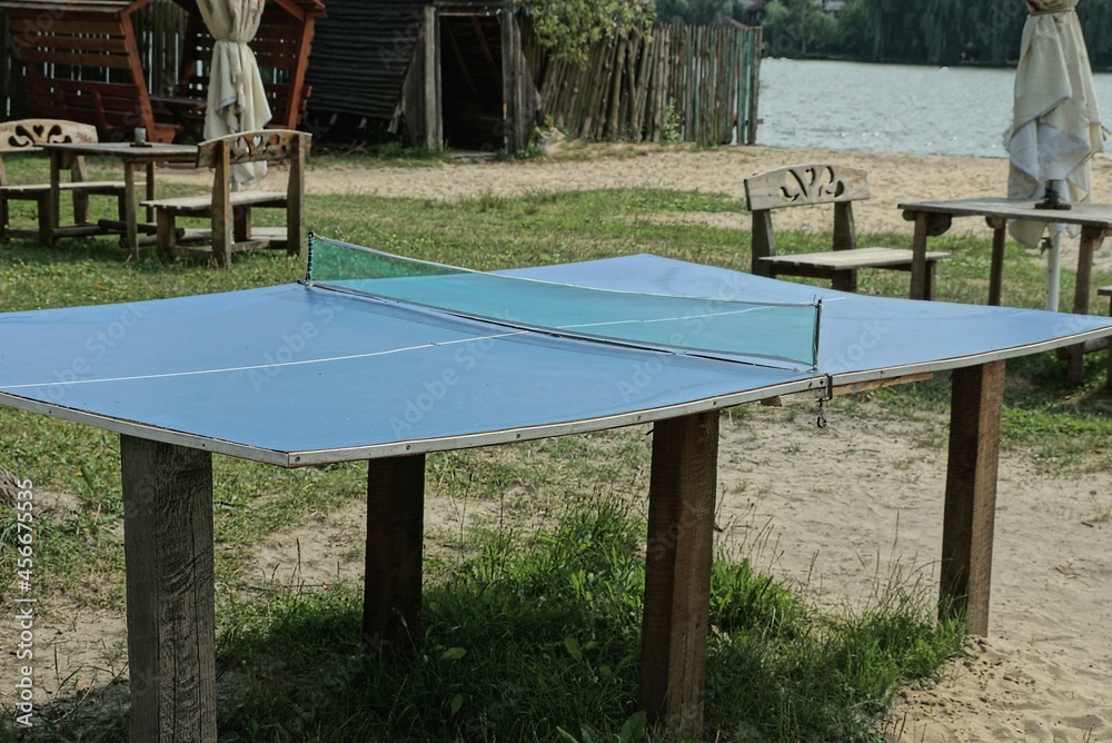 one empty sports blue tennis table outdoors in the grass and sand one empty sports blue tennis table outdoors in the grass and sand