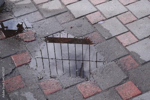 View of a tiled sidewalk with a puddle in which the grid is reflected.