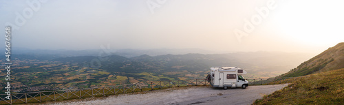 Camper van on road side in beautiful landscape. Dramatic sky at sunset, scenic clouds above unique highlands and hill range in Italy, alternative vanlife vacation concept.