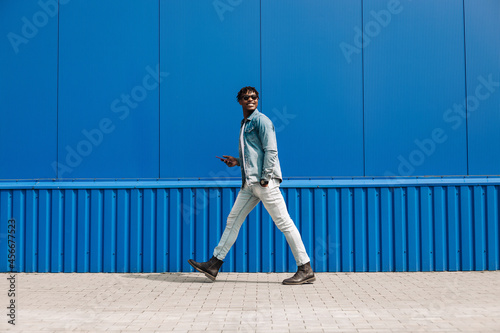 african guy walks with a phone around the city, against the background of a blue building, makes a purchase online