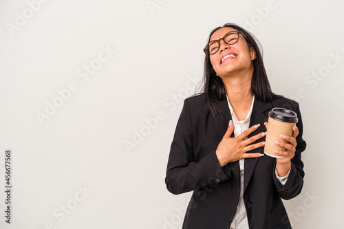 Young business latin woman holding a take away coffee isolated on white background laughs out loudly keeping hand on chest.