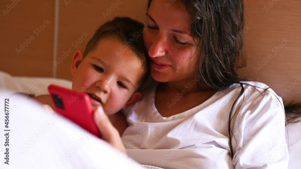 Happy young mother with little son using smart phone together. Mom and little son in bed. High quality 4k footage Happy young mother with little son using smart phone together. Mom and little son in bed. High quality 4k footage