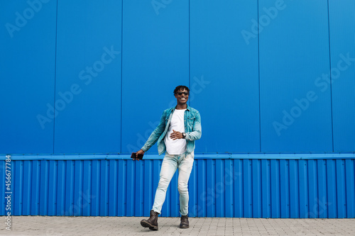 african guy walks with a phone around the city, against the background of a blue building, makes a purchase online