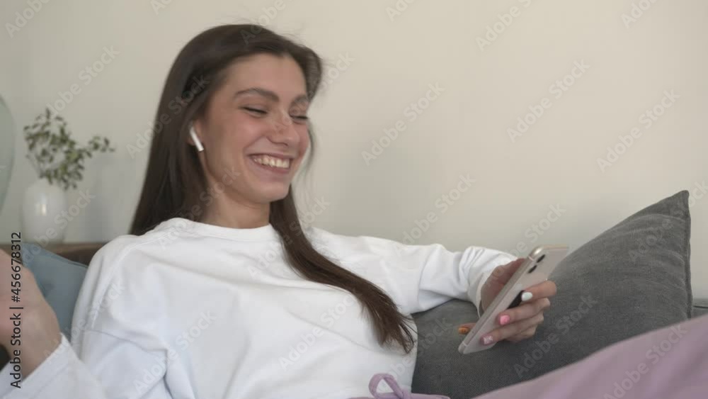 Smiling and beautiful woman enjoying talking on a video call with mobile phone in hand. Caucasian woman in white sweater laughing and chatting at home interior Smiling and beautiful woman enjoying talking on a video call with mobile phone in hand. Caucasian woman in white sweater laughing and chatting at home interior