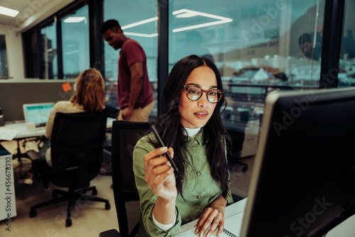 Beautiful multi-ethnic businesswoman concentrating while working on important report essay for boss sitting in office