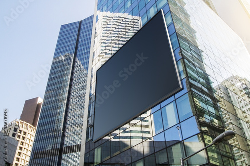 Empty black billboard on glass building in city with bright sky and daylight. Advertisement and commercial concept. Mock up  3D Rendering.
