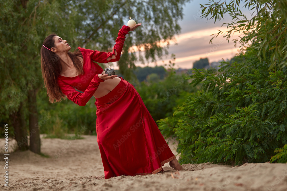 Ritual dance with candles in hands. Brunette woman in red costume for belly-dance is dancing on the beach