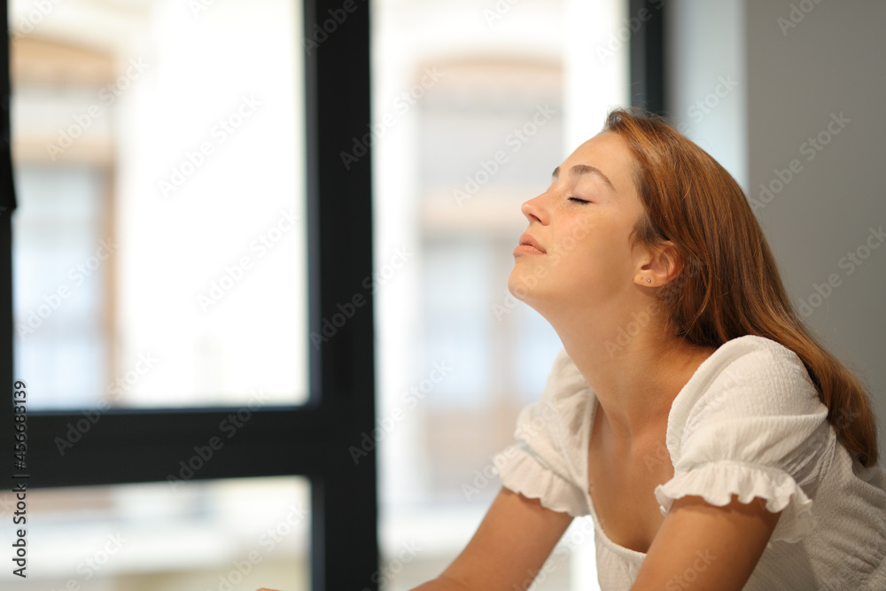 Woman breathing fresh air beside a window at home