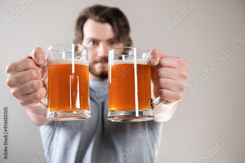 close-up of a young man's hand with two mugs of beer isolated on light gray background