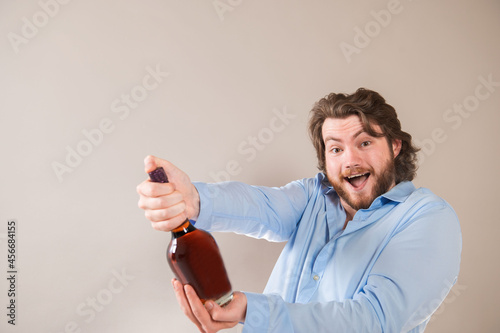  A young happy bearded man holding bottle of cognac isolated on light gray background photo