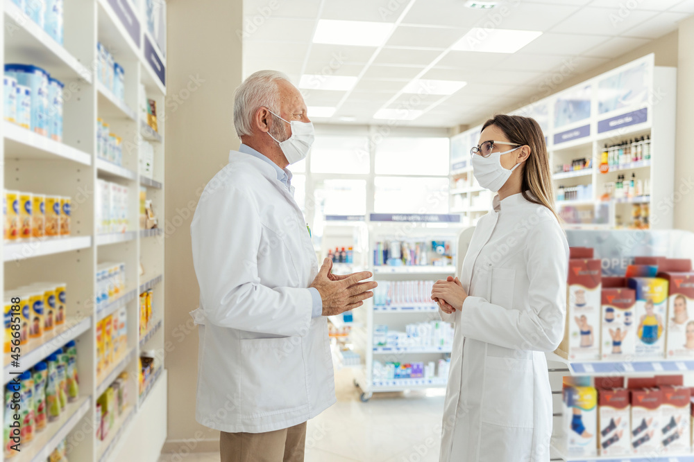 Talking between two pharmacists and the corona virus. Before retiring, the pharmacist teaches the young pharmacist about working in a pharmacy. They wear uniforms and face masks