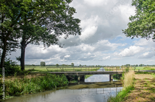 Landscape in the region of Salland in the Netherlands, with trees, meadows, a canal and a simple bridge under a sky with clouds