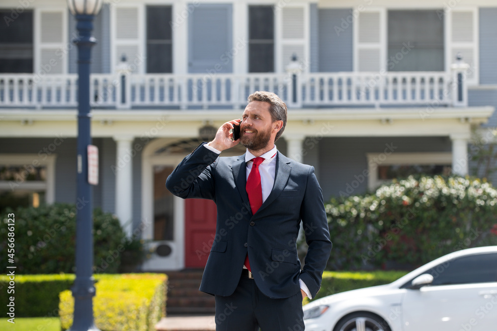 Businessman holding mobile cell phone using app texting sms message wearing suit. Young urban professional man using smartphone at home. Real estate agent.