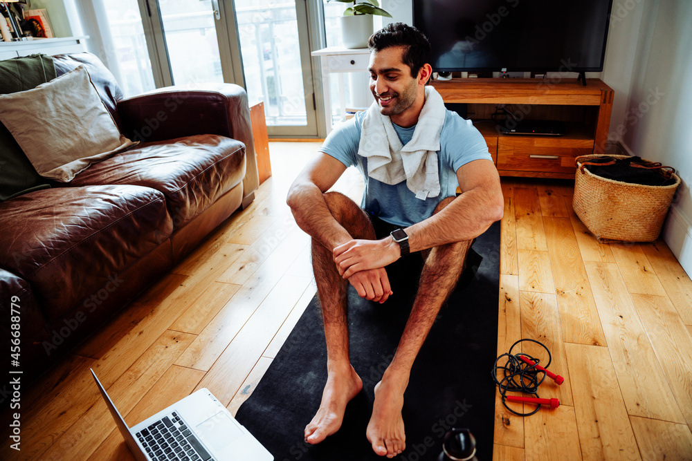 Smiling mixed race male working out from home sitting on floor with sweat  towel looking at laptop Stock Photo | Adobe Stock