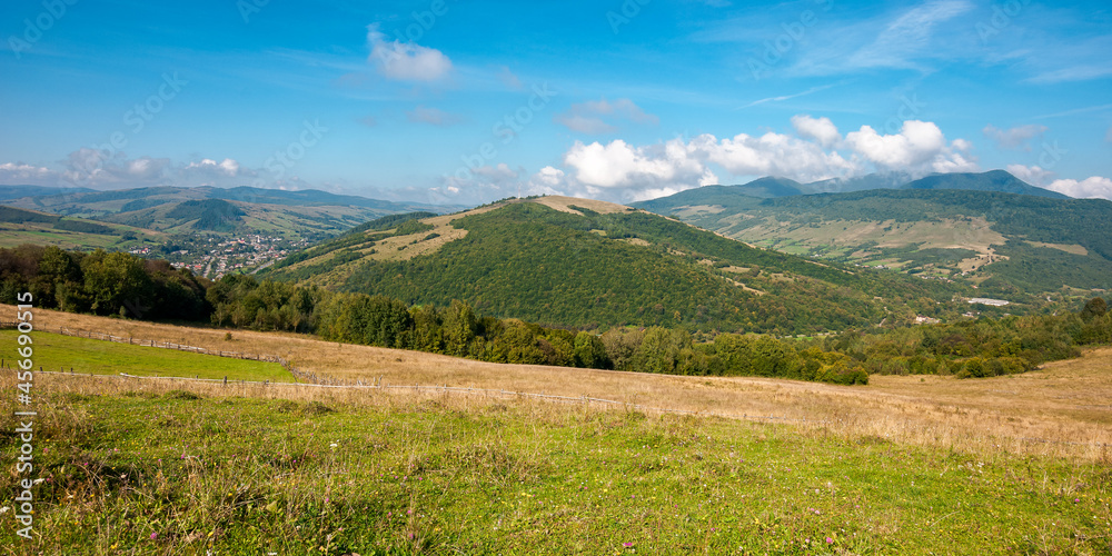 carpathian countryside in september. beautiful mountain landscape with grassy field on the hill. rural scenery with village in the distant valley on a sunny day with clouds on the sky