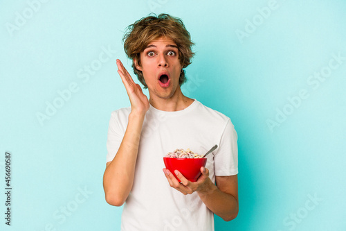 Young caucasian man with makeup a cereal bowl isolated on blue background  surprised and shocked.