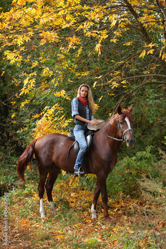 Beautiful cowgirl ride her horse in autumn country road at sunset