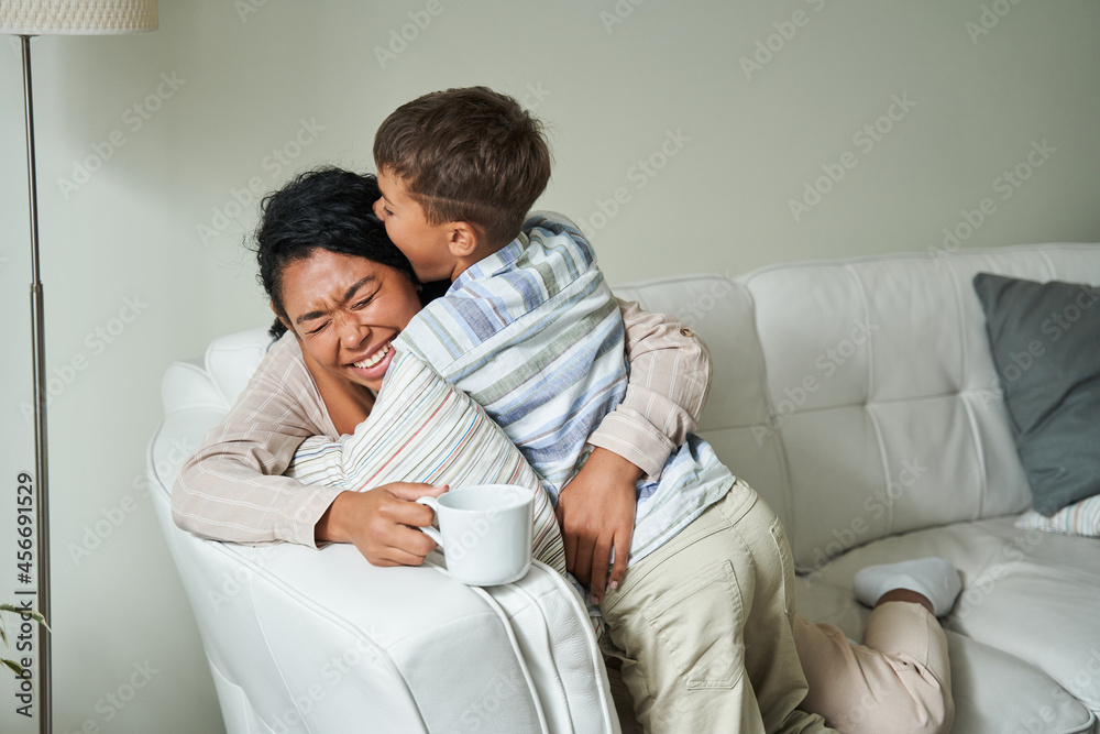 Cute little boy embracing his lovely mother while sitting at the sofa Cute little boy embracing his lovely mother while sitting at the sofa