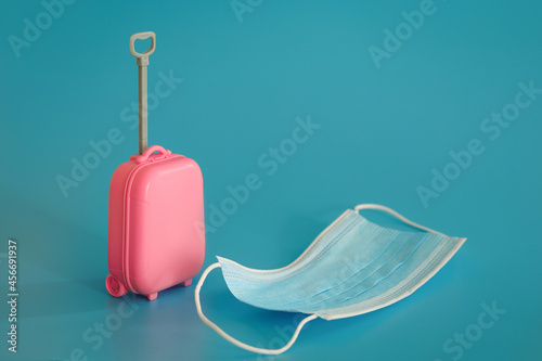 Travel and flights during the time of COVID-19. Mini suitcase, medical mask, coronavirus antigentest on the blue background.  photo