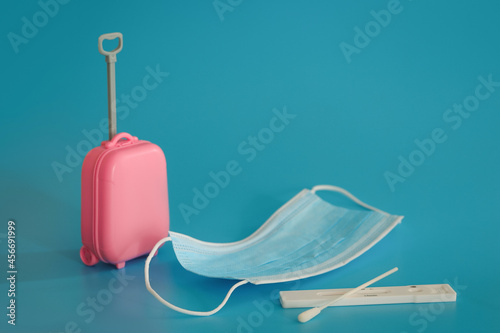 Travel and flights during the time of COVID-19. Mini suitcase, medical mask, coronavirus antigentest on the blue background. Free space, copy space.  photo