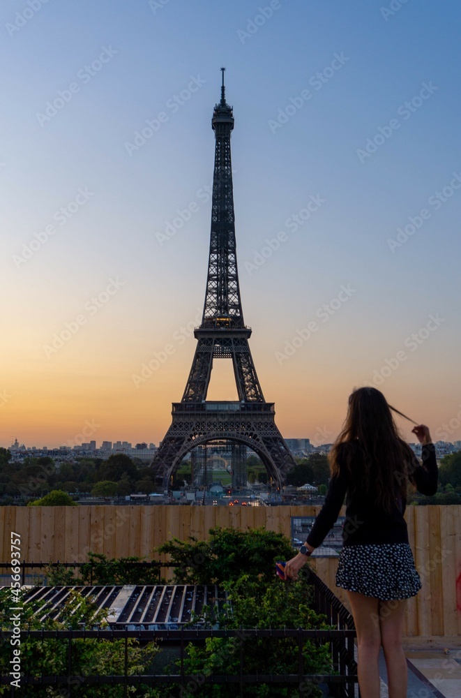 Girl grabbing a lock of hair while looking at the Eiffel Tower at cloudless sunrise