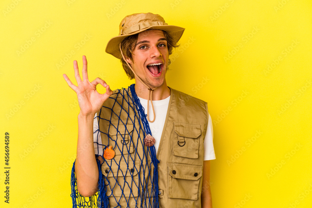 Young fisherman with makeup holding a net isolated on yellow background cheerful and confident showing ok gesture. Young fisherman with makeup holding a net isolated on yellow background cheerful and confident showing ok gesture.
