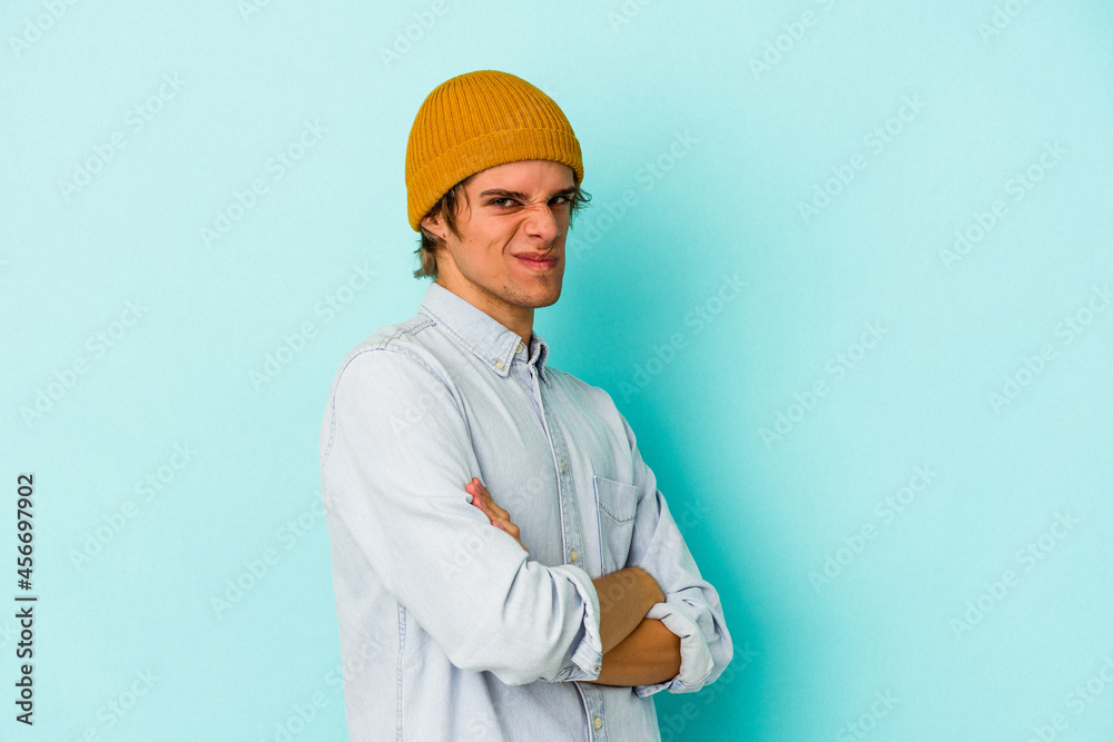 Young caucasian man with make up isolated on blue background frowning face in displeasure, keeps arms folded. Young caucasian man with make up isolated on blue background frowning face in displeasure, keeps arms folded.