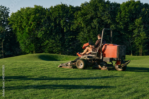 Greenkeeper. Golf course maintenance worker, cutting green grass photo