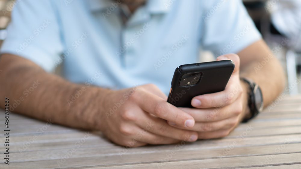 Man chatting in the restaurant. Man holding phone. Black smartphone in hand on wooden table