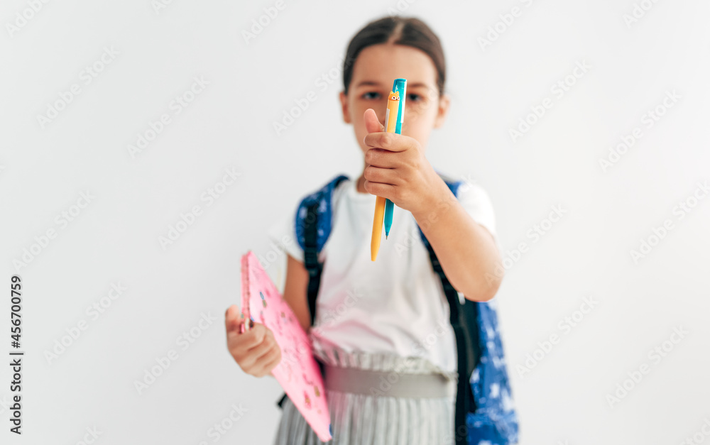Portrait of a little girl with backpack showing a pencil in focus directly to the camera. School kid with backpack going back to school. Portrait of a little girl with backpack showing a pencil in focus directly to the camera. School kid with backpack going back to school.