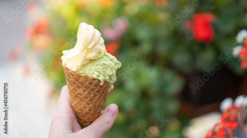 Hand holding double color ice cream in cone on street. Best gelato cone. Pistachio gelato. Mango ice cream