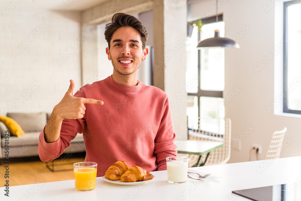 Young mixed race man having breakfast in a kitchen on the morning person pointing by hand to a shirt copy space, proud and confident Young mixed race man having breakfast in a kitchen on the morning person pointing by hand to a shirt copy space, proud and confident