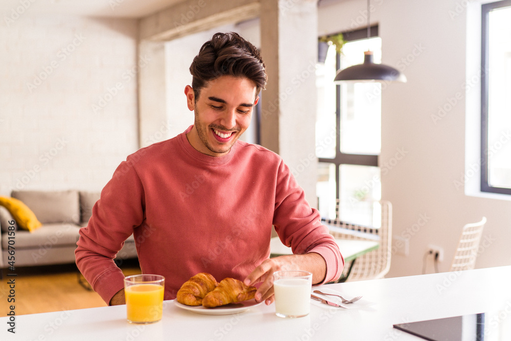 Young mixed race man eating croissant in a kitchen on the morning Young mixed race man eating croissant in a kitchen on the morning