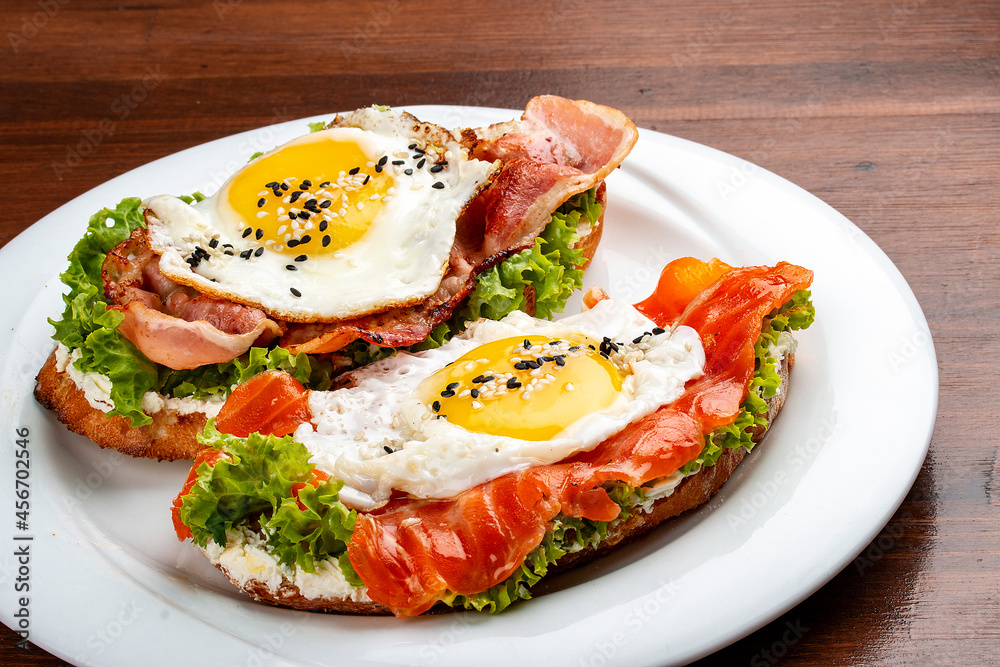 Toast with salmon, bacon and cream cheese. On a wooden background. Breakfast Toast with salmon, bacon and cream cheese. On a wooden background. Breakfast
