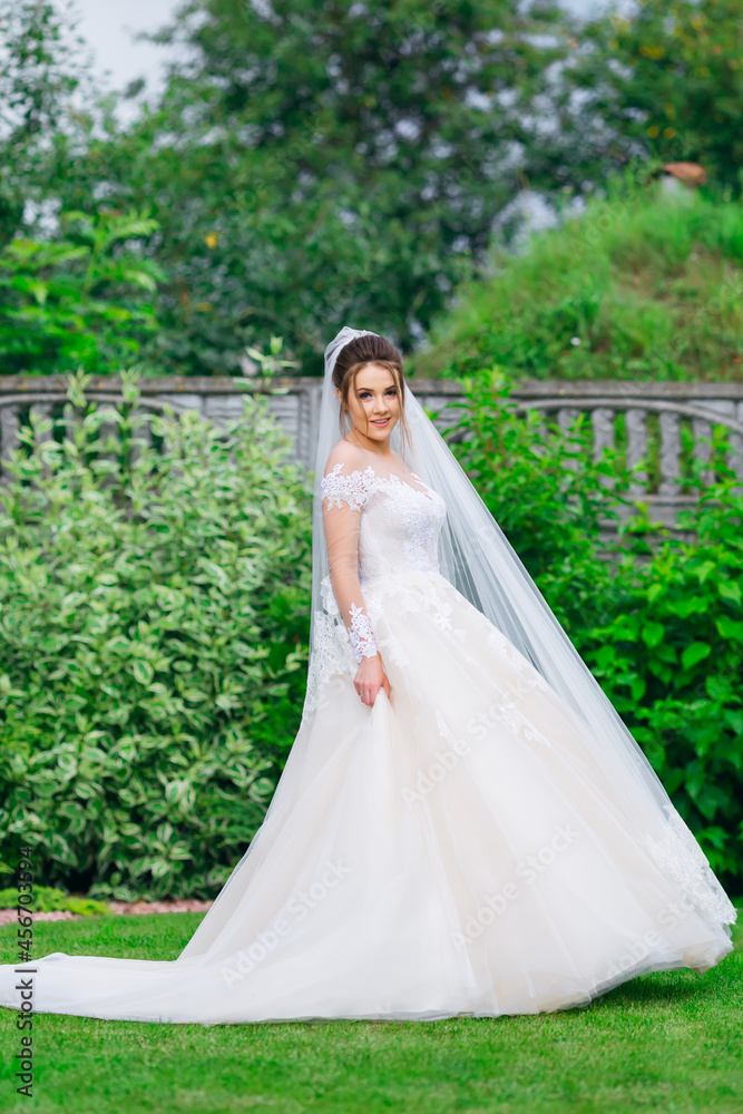 Happy young bride in a delicate white wedding dress in the summer garden, before the ceremony