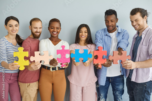 Fotografie Studio group portrait of six happy smiling multiethnic young people joining big colorful jigsaw puzzle pieces