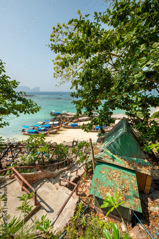 Naklejka premium Stairs going down to a beach with long tail boats on Phi Phi island next to a bungalow with green roofs