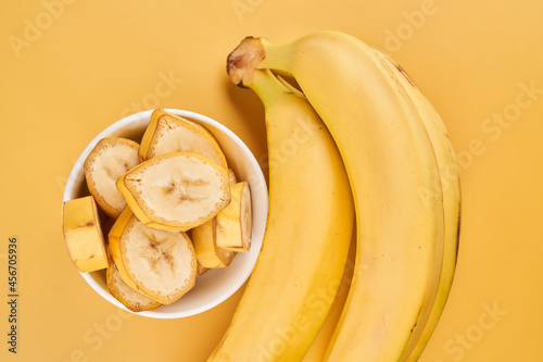 White cup with sliced bananas on a yellow background. Tropical fruits, healthy food, vitamins