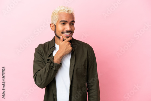 Young Colombian handsome man isolated on pink background looking to the side and smiling