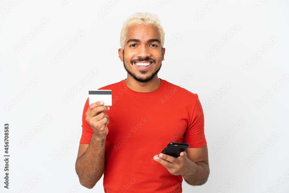 Young Colombian handsome man isolated on white background buying with the mobile with a credit card Young Colombian handsome man isolated on white background buying with the mobile with a credit card